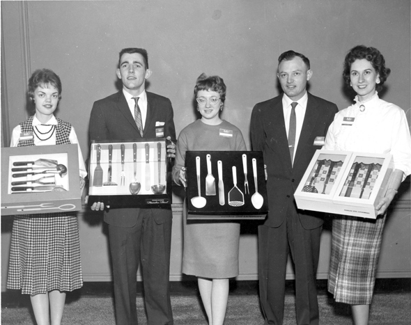 Two men and three woman in business attire holding display boxes of cooking utensils
